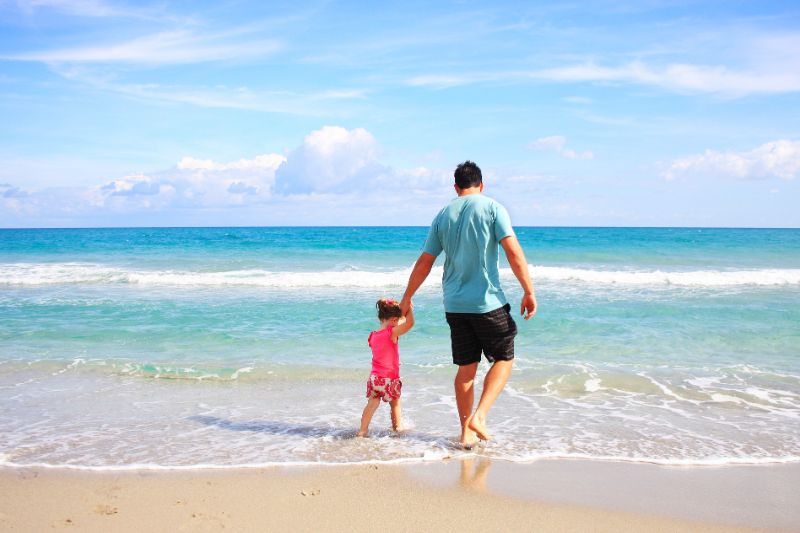 Ein Vater und seine Tochter wandern am Strand entlang.